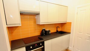 Eine Küche mit weißen Schränken, einer orangefarbenen Fliesenspiegel, einer schwarzen Arbeitsplatte, einem Herd und einem Backofen.