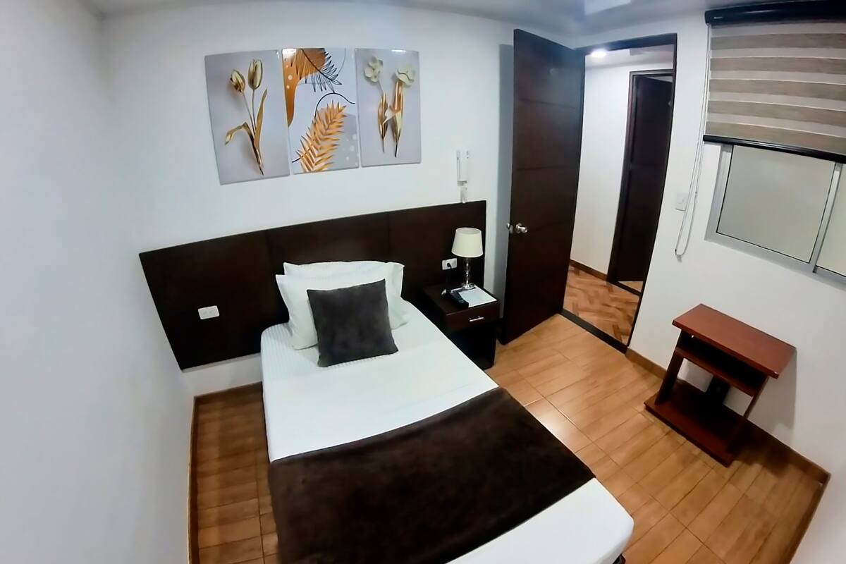 A neatly arranged bedroom with a bed, bedside table, lamp, and artwork on the wall.