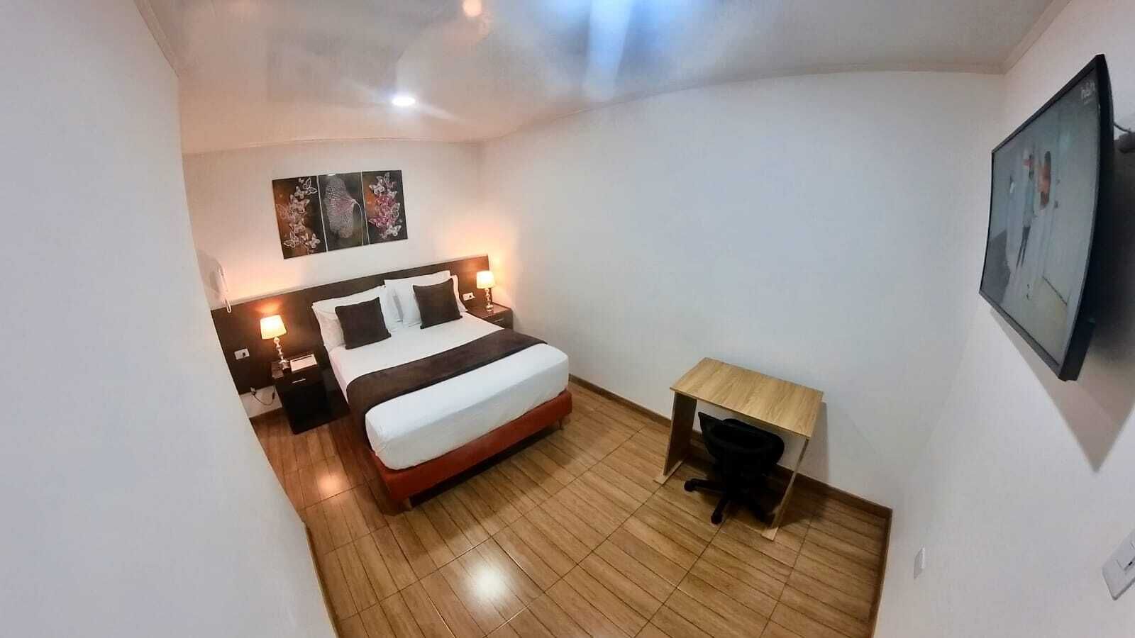 Um quarto com cama, mesas de cabeceira, escrivaninha e uma cadeira.