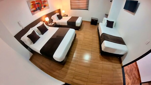 A hotel room with two beds, a flat-screen TV, a bedside table with a lamp, and a wooden floor. - Hotel victoria Real (Tunja)