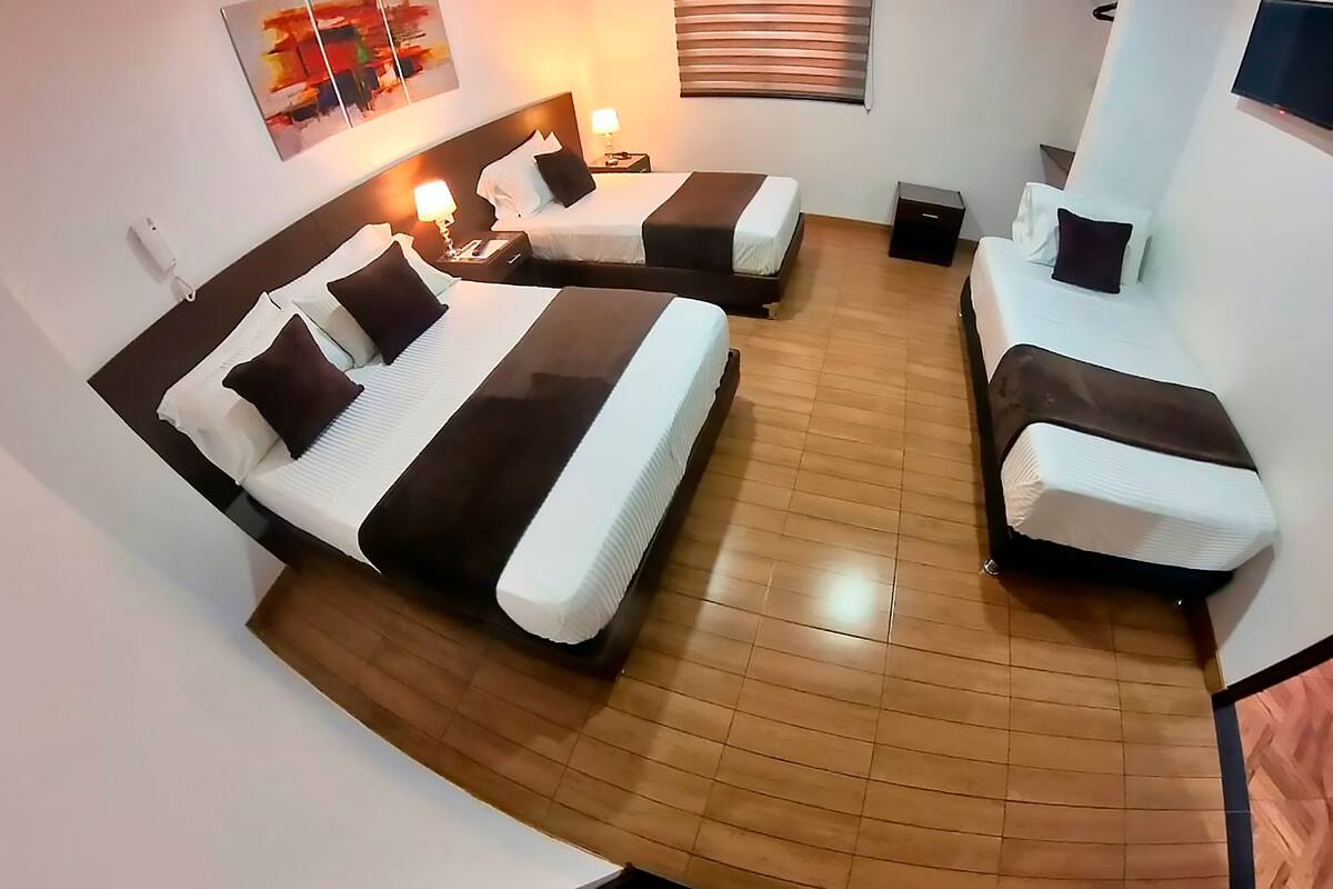 A hotel room with two beds, a flat-screen TV, a bedside table with a lamp, and a wooden floor.
