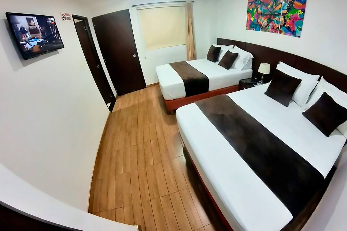 A hotel room with a large bed, a smaller sofa, a TV, a door, and a window.