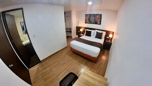A hotel room with a bed, bedside lamps, a small table, and a mirror. - Hotel victoria Real (Tunja)
