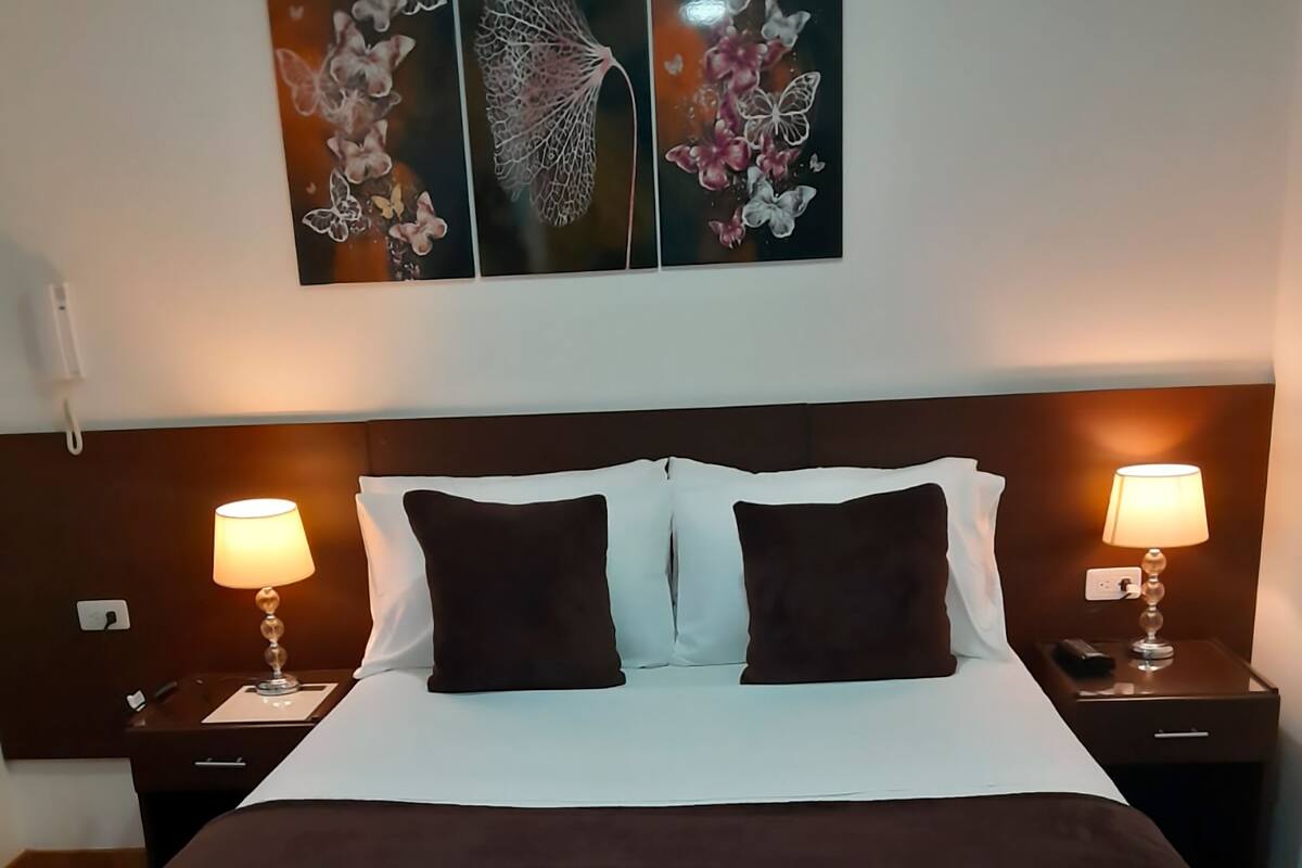 A hotel room with a large bed, two bedside tables with lamps, a headboard, and three wall-mounted artworks depicting butterflies and flowers.