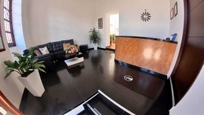 A spacious lobby with a black leather sofa, a reception desk, and a potted plant. - Hotel victoria Real (Tunja)