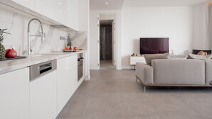 Een moderne keuken met witte kasten, een roestvrijstalen spoelbak en een flatscreen televisie in de woonkamer.