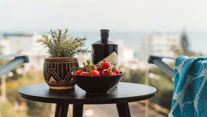 Een balkon met een kleine tafel waarop een bloempot en een schaal aardbeien staan, met een stadszicht op de achtergrond.