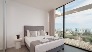 Een moderne hotelkamer met een groot bed, een nachtkastje en een prachtig uitzicht op de stad door grote ramen.