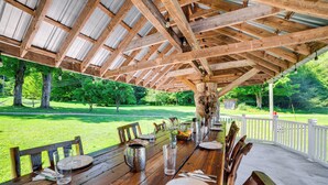 Une table à manger en bois installée à l’extérieur, avec vue sur une zone herbeuse et des arbres.