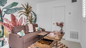 Ein Wohnzimmer mit einem braunen Sofa, einem Holztisch und einer großen Wandmalerei mit tropischen Blättern.