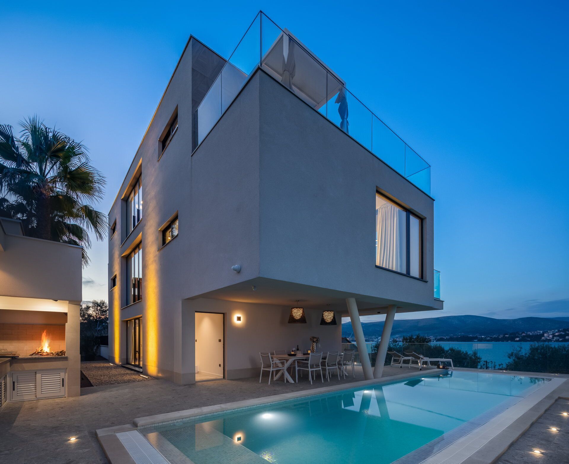 A modern two-story house with a swimming pool, outdoor seating, and a view of the mountains.