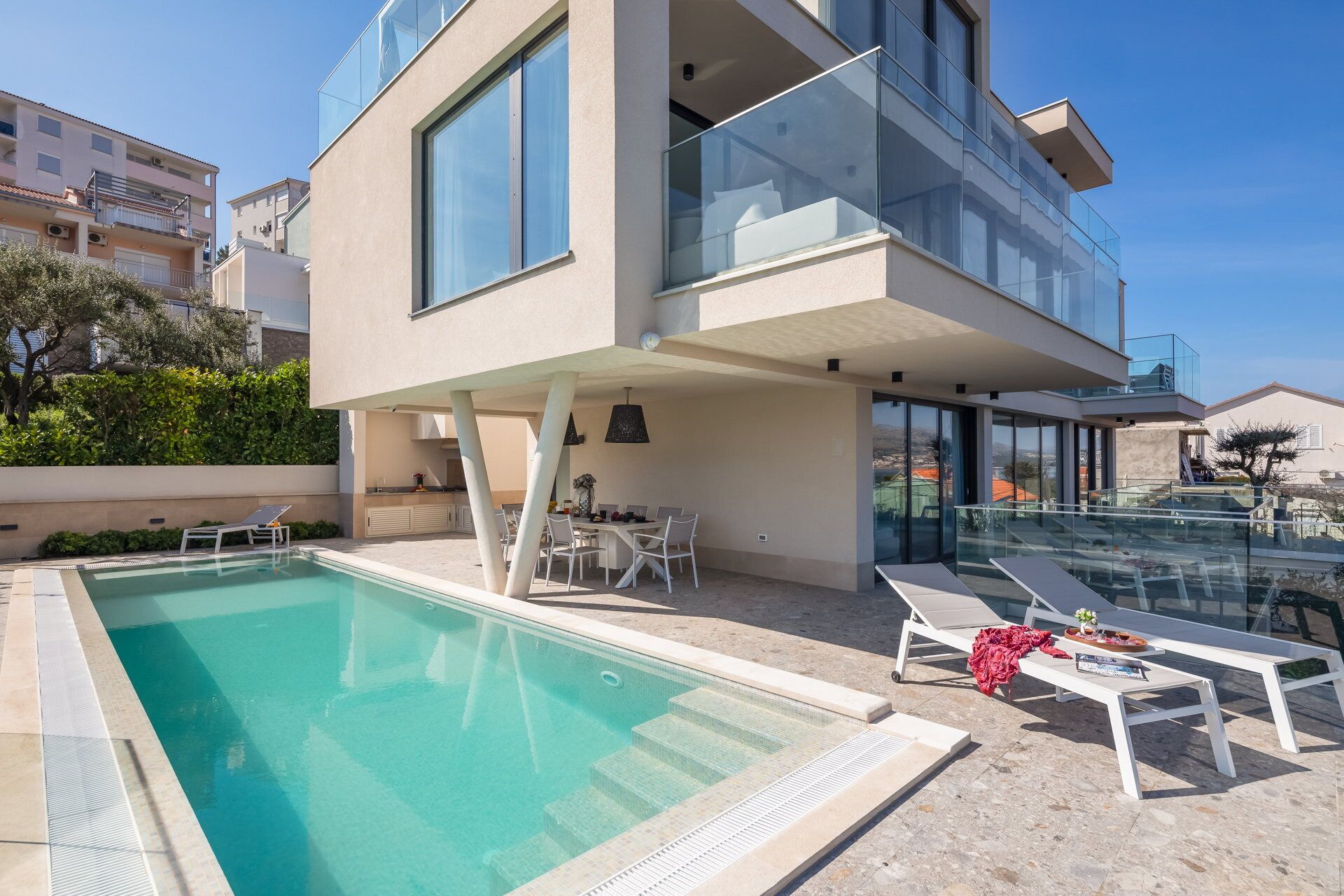 A modern two-story building with a swimming pool, outdoor seating, and a glass balustrade.