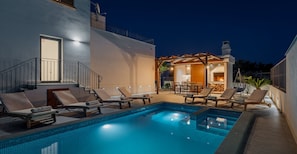A swimming pool with lounge chairs, a covered outdoor seating area, and a fire pit.