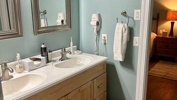 A bathroom with two sinks, a mirror, a hairdryer, and a trash can.