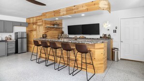 A modern kitchen with a wooden island, bar stools, a large TV, and a ceiling fan. - Lakeside Lodge - Game Cave, Golf Greens! Sleeps 17 (Gladwin)