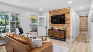 A modern living room with a leather sofa, a wooden cabinet, and a flat-screen TV mounted on the wall. - Lakeside Lodge - Game Cave, Golf Greens! Sleeps 17 (Gladwin)