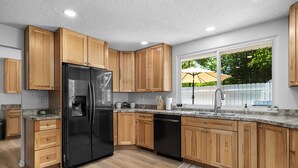 A modern kitchen with wooden cabinets, a black refrigerator, and a dishwasher. - Lakeside Lodge - Game Cave, Golf Greens! Sleeps 17 (Gladwin)