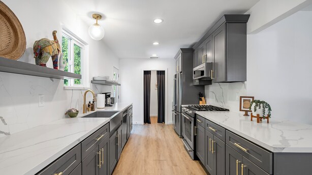 Una cocina moderna con armarios gris oscuro, encimeras de mármol blanco y suelo de madera.