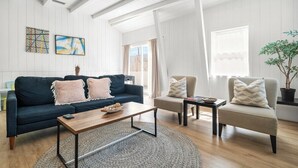 Un salón moderno con un sofá azul oscuro, un sillón gris claro y una mesa de centro de madera. Se observan obras de arte abstracto en las paredes y una planta en maceta.