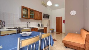 A compact kitchen with wooden cabinets, a dining table with a blue tablecloth, and a sofa in the living area.