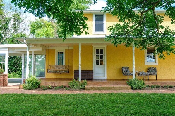 A yellow house with a covered porch, a front door, and two windows.
