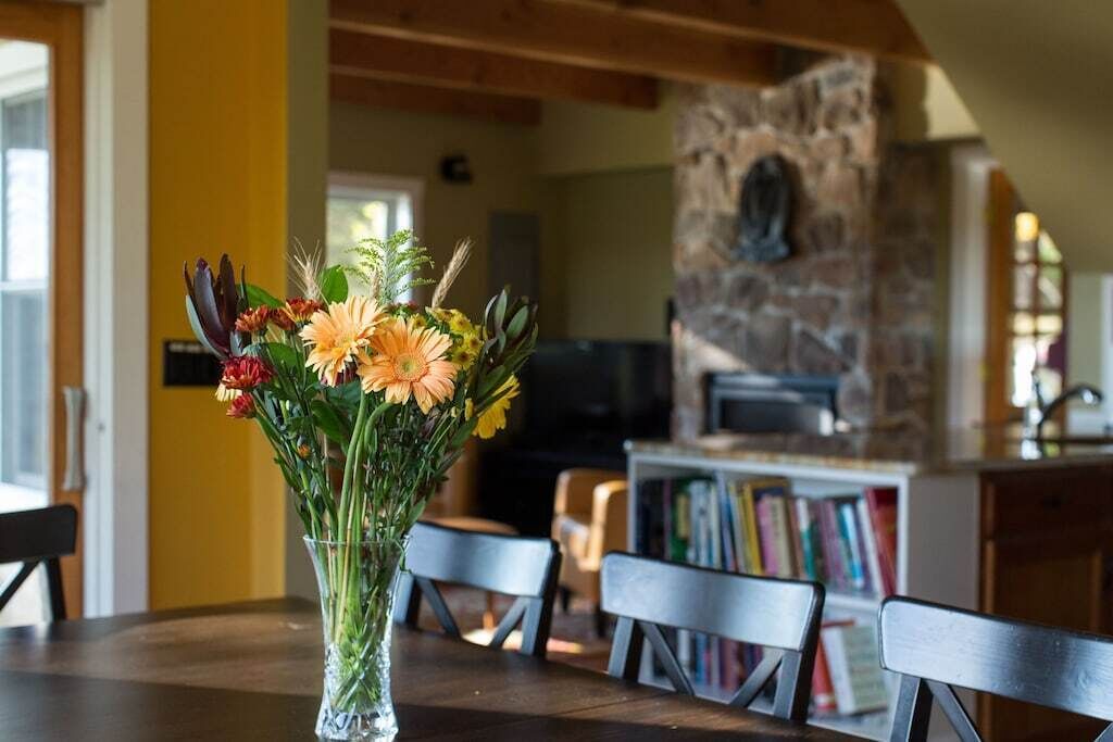 Un coin repas avec une table dressée pour deux personnes, un vase de fleurs et une cheminée en pierre en arrière-plan.
