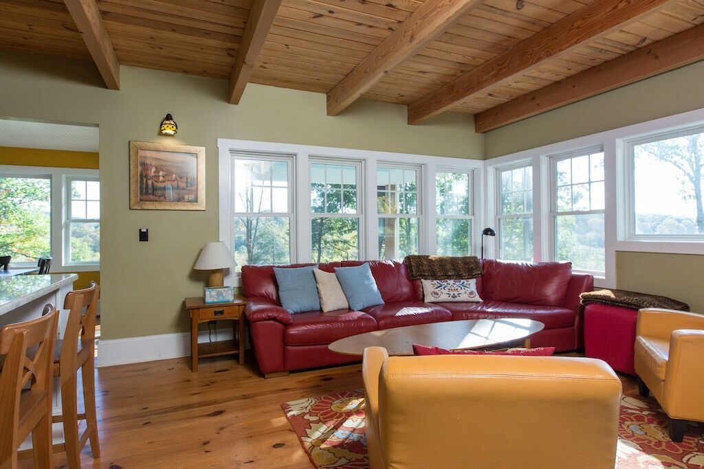 A cozy living room with a red leather sofa, yellow armchairs, and a wooden ceiling.