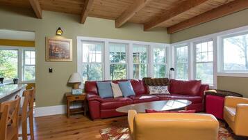 A cozy living room with a red leather sofa, yellow armchairs, and a wooden ceiling.