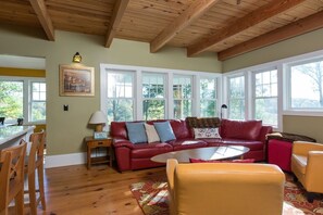 A cozy living room with a red leather sofa, yellow armchairs, and a wooden ceiling.