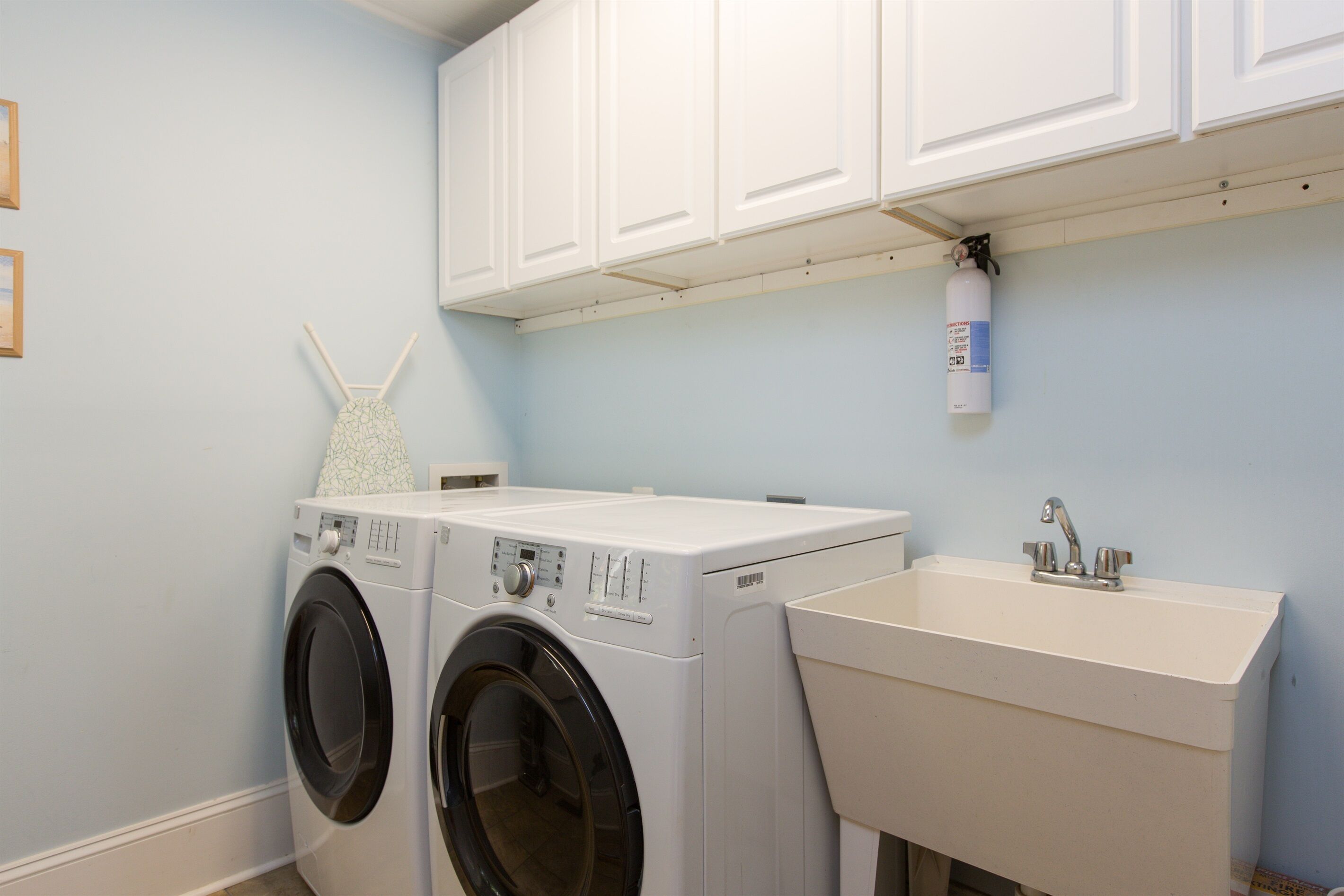 A laundry room with two front-loading washing machines, a sink, and a fire extinguisher mounted on the wall.