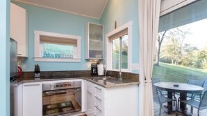 A kitchen with white cabinets, a built-in oven, a window with a view of a green landscape, and a dining area with a table and chairs. - Fantasy Cottage: Private Pond, Waterfall, Hot Tub (Front Royal)