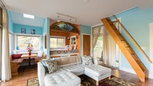 A spacious living room with a white sectional sofa, a wooden staircase, and a view of the outdoors. - Fantasy Cottage: Private Pond, Waterfall, Hot Tub (Front Royal)