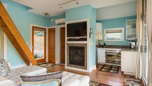 A modern living room with a fireplace, a kitchen with white cabinets, and a staircase. - Fantasy Cottage: Private Pond, Waterfall, Hot Tub (Front Royal)