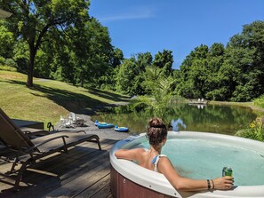 A hot tub on a wooden deck with a view of a lake and trees.