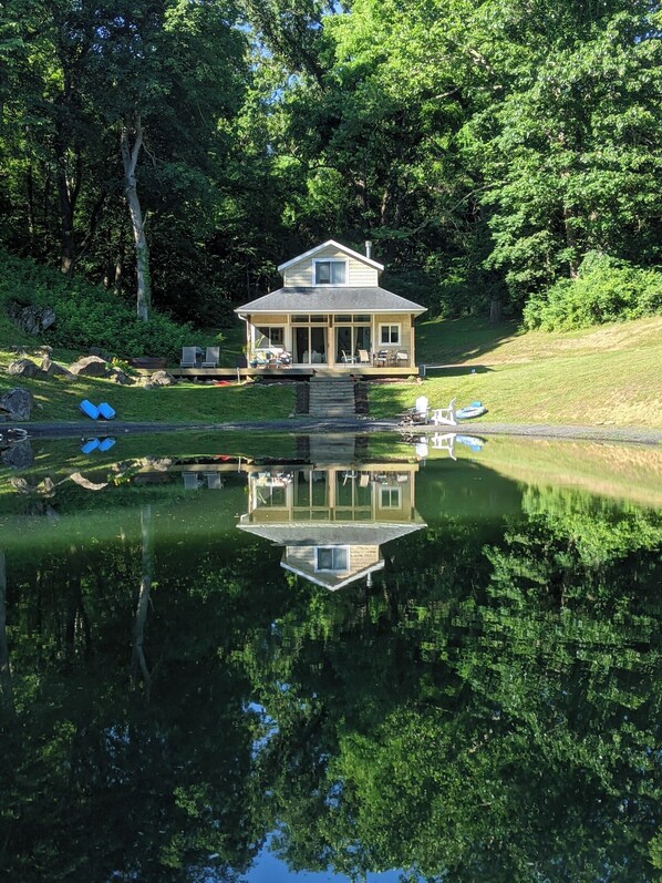 A house with a reflection in a pond, surrounded by trees.