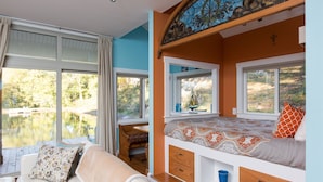 A cozy room with a bed, a sofa, and a window overlooking a lake. - Fantasy Cottage: Private Pond, Waterfall, Hot Tub (Front Royal)