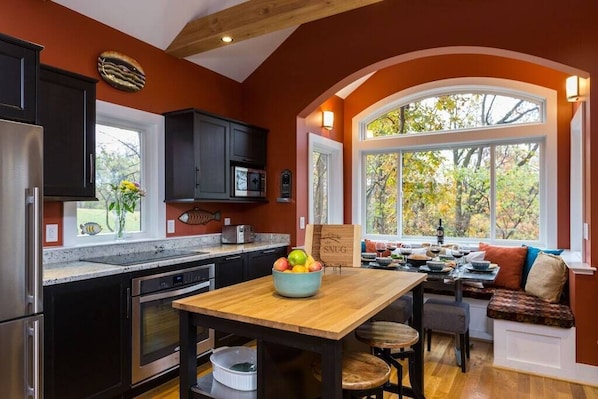 Une cuisine avec des meubles de couleur sombre, une table en bois et une fenêtre donnant sur un jardin.