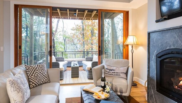 Una sala de estar acogedora con chimenea, un sofá, una silla y una mesa con un libro y aperitivos.