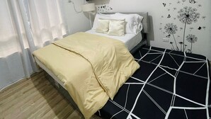 Een slaapkamer met een bed, nachtkastje, wandheater, raam met gordijnen en een schilderij aan de muur.