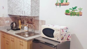 Een kleine keuken met een marmeren kastje, een magnetron en een vaatwasser. Er zijn houten kastjes, een spoelbak en een aanrecht.