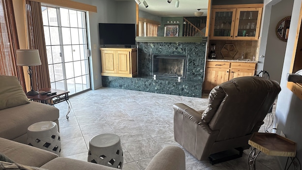 A spacious living room with a leather recliner, a sofa, and a coffee table. A fireplace is visible in the background, and there is a kitchen area with wooden cabinets. - Riverfront 2 bed/2.5 bath Condo w/ Pool & Spa, River Dock - Small Dogs OK! (Bullhead City)