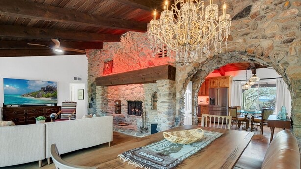 Un vaste espace de vie agrémenté d’une cheminée en pierre, de meubles en bois et d’un grand lustre.