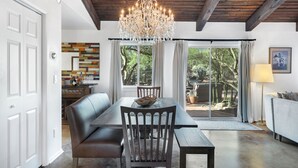 Un espace repas agrémenté d’un lustre, de poutres en bois au plafond, d’une table à manger, de chaises et offrant une vue sur l’extérieur grâce à de grandes fenêtres.