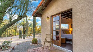 Un bâtiment de style désertique avec une terrasse en briques, une chaise en bois et un jardin de cactus.