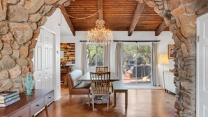 Une pièce spacieuse avec une arche en pierre, un plafond en bois, un lustre, une table à manger avec des chaises et une vue dégagée sur l’extérieur grâce à de grandes fenêtres.