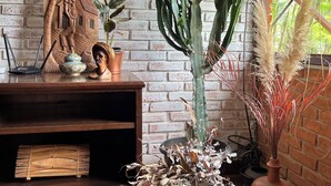 Una habitación rústica con pared de ladrillo, un cactus, objetos decorativos y una ventana con vistas a follaje.