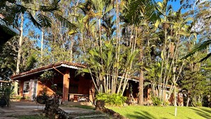 Una casa rústica con techo rojo y paredes de piedra, rodeada de exuberante follaje y palmeras.