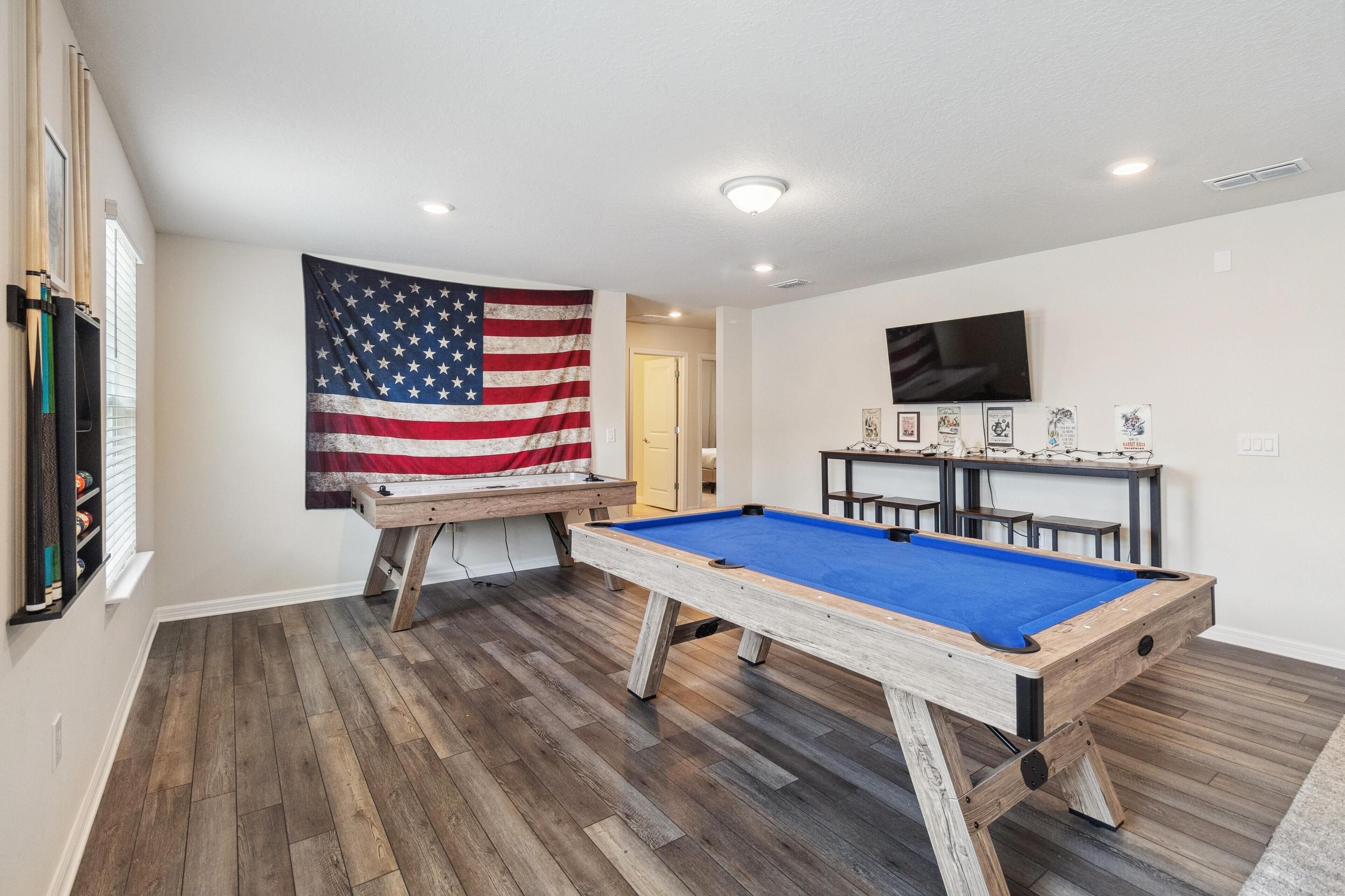 A room with a pool table, a billiards table, and an American flag.