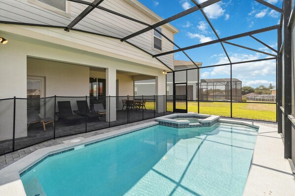 A swimming pool with a hot tub, surrounded by a covered patio with chairs and a table.