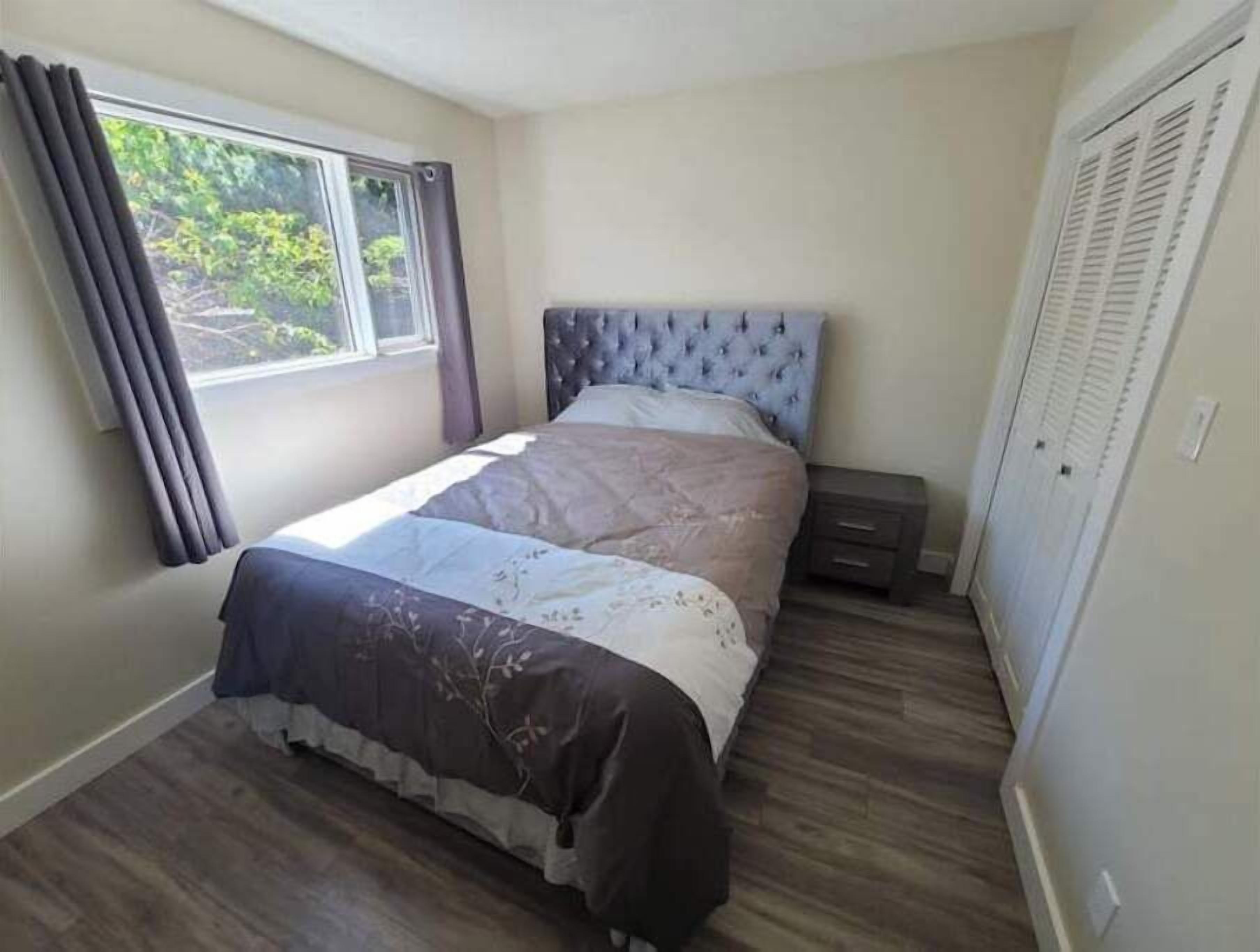 Un dormitorio con cama, mesita de noche, ventana con cortinas y armario.